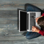 Person using laptop on wooden floor.