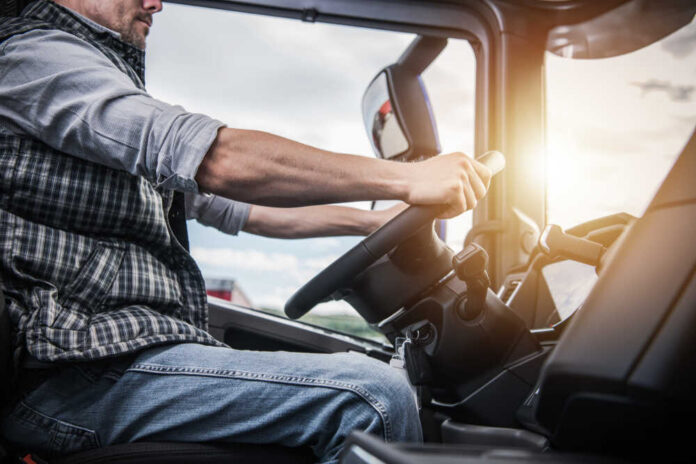 A truck driver gripping the steering wheel inside a vehicle cabin