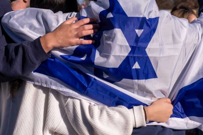 Israeli flag with arms_2388929731.jpg People holding an Israeli flag together, showcasing unity and cultural pride