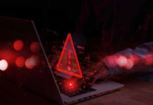 Red warning triangle on computer screen, hands typing.