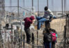 People climbing barbed wire fence wearing backpacks and hoodies