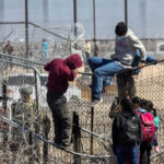 People climbing barbed wire fence wearing backpacks and hoodies