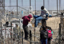 People climbing barbed wire fence wearing backpacks and hoodies