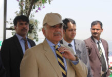 A group of men in formal attire at an outdoor event, with one man wearing a cap