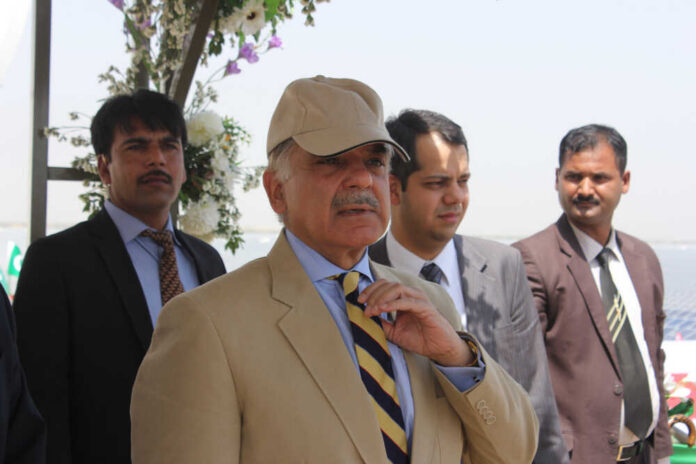A group of men in formal attire at an outdoor event, with one man wearing a cap