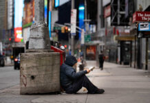 A person sitting against a concrete pillar reading a book in an urban setting
