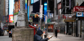 A person sitting against a concrete pillar reading a book in an urban setting