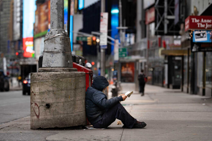A person sitting against a concrete pillar reading a book in an urban setting