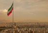 Iranian flag waving over a city skyline with mountains in the background