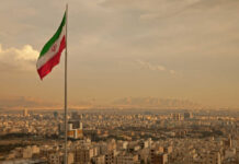 Iranian flag waving over a city skyline with mountains in the background