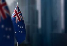 Australian flag displayed on a flagpole with a blurred city background
