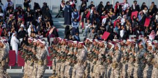 Soldiers in military uniforms marching in a parade with a crowd in the background