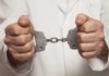 A person in a white coat holding handcuffs tightly