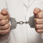 A person in a white coat holding handcuffs tightly