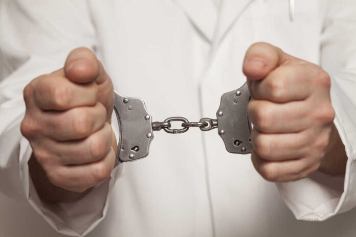 shutterstock_271047269.jpg A person in a white coat holding handcuffs tightly