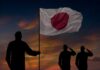 Silhouettes of soldiers saluting the Japanese flag against a sunset