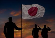 Silhouettes of soldiers saluting the Japanese flag against a sunset