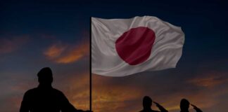 Silhouettes of soldiers saluting the Japanese flag against a sunset