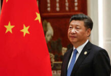 Man in suit standing beside Chinese flag indoors.