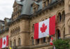 Historic building with large Canadian flags displayed outside