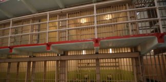 Prison cell block interior with barred doors and dull lighting.