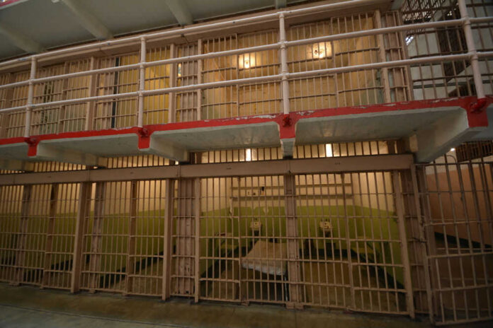 Prison cell block interior with barred doors and dull lighting.