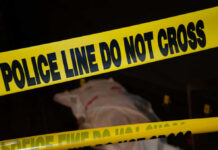 Police tape with indistinct body underneath in shadowed area