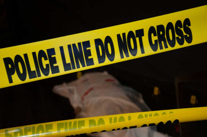 Police tape with indistinct body underneath in shadowed area