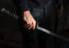 A close-up of a hand gripping a katana sword against a dark background