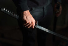 A close-up of a hand gripping a katana sword against a dark background
