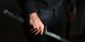A close-up of a hand gripping a katana sword against a dark background