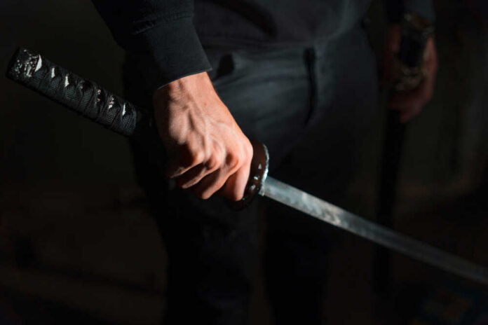 A close-up of a hand gripping a katana sword against a dark background