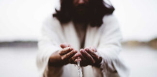Person in white robes pouring water from their hands