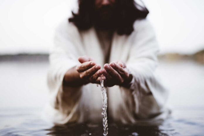 Person in white robes pouring water from their hands