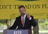 A man delivering a speech at an outdoor event with a 'Don't Tread on Florida' banner in the background