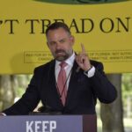 Explosive Allegations: Mills’ Troubling Legal Battles A man delivering a speech at an outdoor event with a 'Don't Tread on Florida' banner in the background