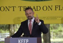 A man delivering a speech at an outdoor event with a 'Don't Tread on Florida' banner in the background