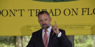 A man delivering a speech at an outdoor event with a 'Don't Tread on Florida' banner in the background
