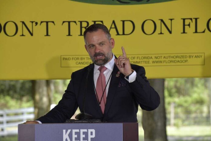A man delivering a speech at an outdoor event with a 'Don't Tread on Florida' banner in the background