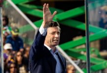 A man in a suit gesturing while speaking at an outdoor event