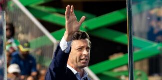 A man in a suit gesturing while speaking at an outdoor event