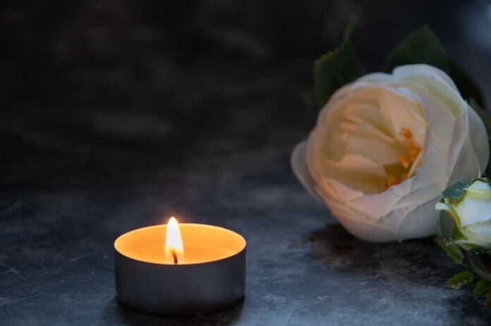A lit candle beside a white flower on a dark surface