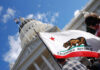 California state flag held up in front of a government building under a blue sky