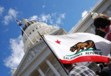 California state flag held up in front of a government building under a blue sky