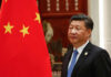 Man in suit standing beside Chinese flag indoors.