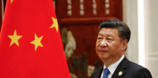 Man in suit standing beside Chinese flag indoors.