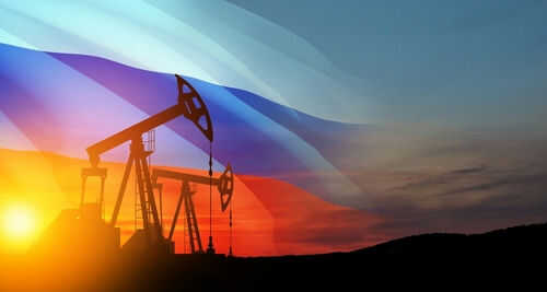 2212276215 Oil pumps silhouetted against Russian flag and sunset.