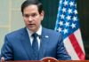 Rubio Secures Deportation Deals With 20+ Countries A man in a blue suit speaking into a microphone with an American flag in the background