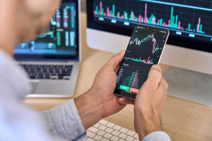 cryptoplatformid2158971843jpg-1 Person checking stock market graphs on phone and monitors.