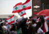 Crowd holding Lebanese flags and umbrellas in city.